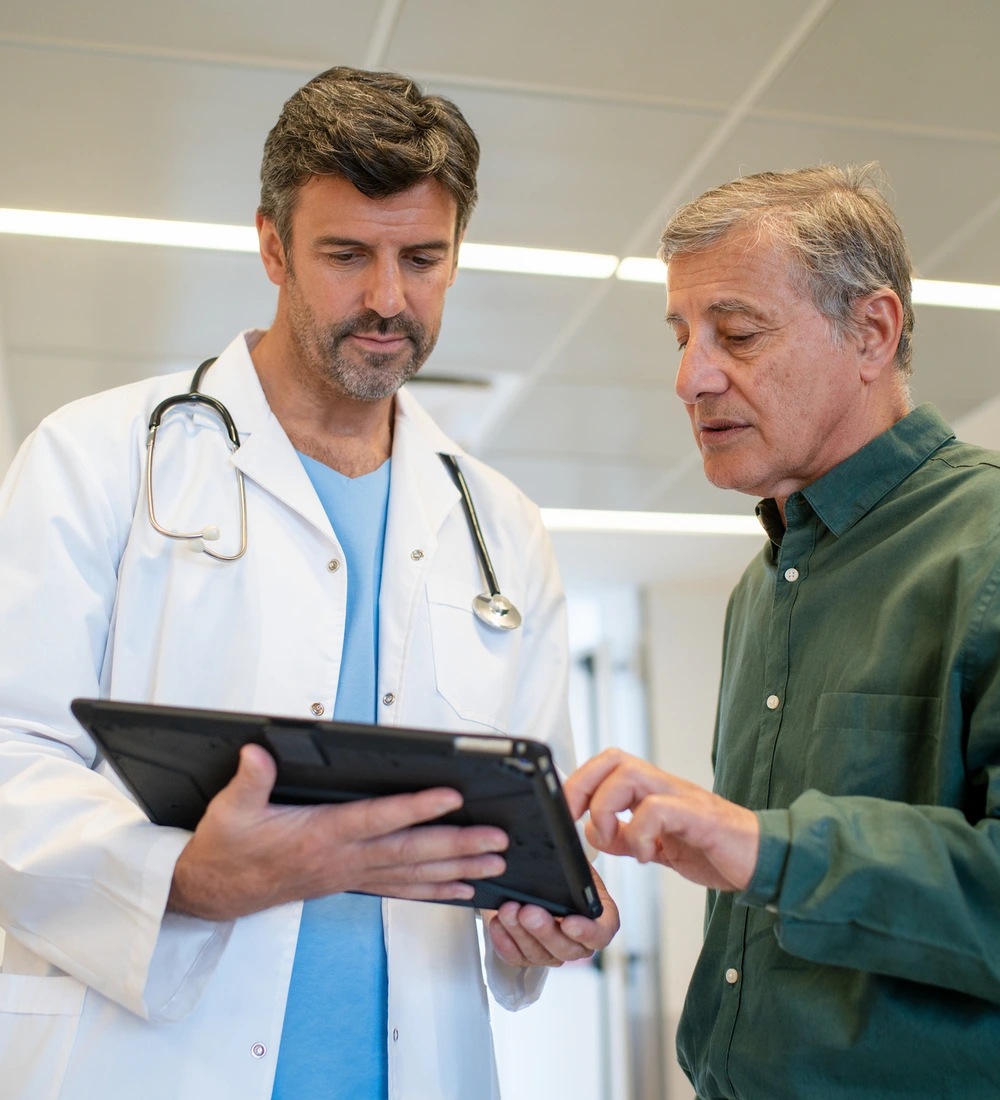 Cirujano vascular conversando con un paciente mientras revisan sus resultados en una tablet